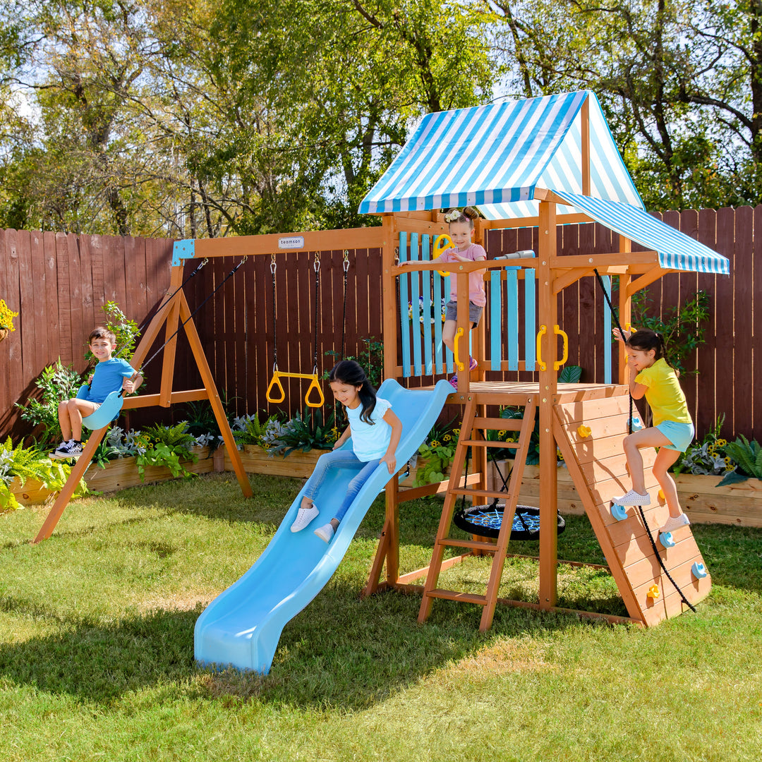 4 kids playing on the blue outdoor swing set in the backyard.